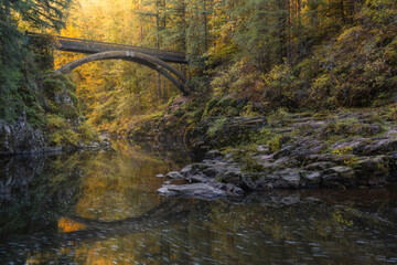 Scenic bridge reflecting over calm river water in beautiful enchanted autumn forest landscape
