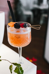 Glass of orange cocktail decorated with red berries at bar.