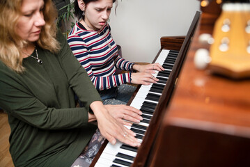 Mom and daughter play piano at home four hands, study a new piece of music, the teenage girl does not play well and is angry, but still studies further, the focus is on girl's fingers