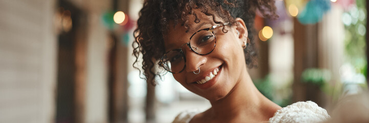 Closeup portrait of a young woman in glasses smiling poses and sends an air kiss on a smartphone selfie camera. Positive woman using mobile phone outdoors in urban background