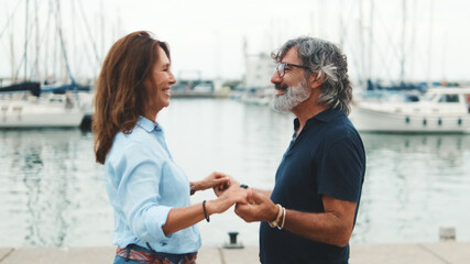 Happy middle aged couple smiling confidently dancing in the marina on the yachts background