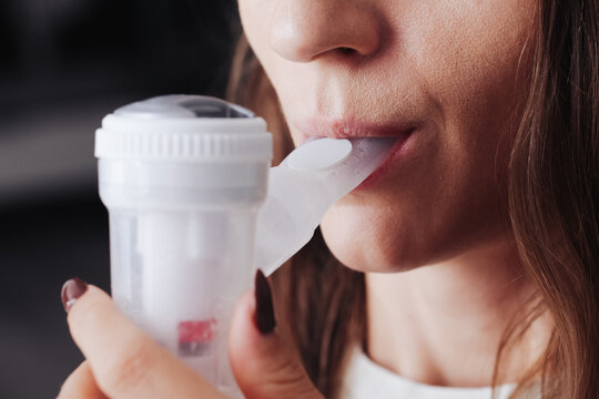 Nebulizer device in mouth. Woman with inhaler in her mouth background. Breathing saline through nebulization. Mouth inserted nebulizer. Lung and throat treatment.