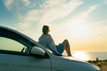 Solo traveler woman lie on car and enjoy beautiful sunset on seacoast. Travel by car