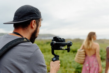 young man records video with his camera installed on a gimbal to a group of girls on the beach. filmamaker works filming outdoors