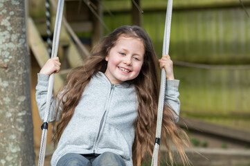 A little girl with long wavy hair swinging on the garden swing in the backyard, green fence on the background, selective focus