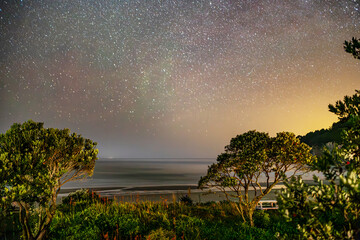 Beautiful star trails light up the night sky of Whangamata in New Zealand - obrazy, fototapety, plakaty