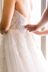 A bride is getting ready, putting on her wedding dress with someone else helping her.