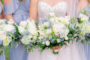 A bride and bridesmaids in blue dresses holds a white bouquet with blue flowers. 