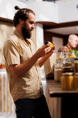 Man in zero waste store taking time to analyze juice, making sure it's made from organic fruits. Customer thoroughly checking food items are safe in environmentally responsible local supermarket - obrazy, fototapety, plakaty