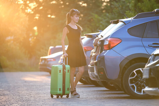 Young Woman Driver Taking Out Suitcase Bag Out Of Her Car. Travelling And Vacations Concept