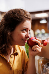 Hipster woman smelling bio farm grown apples in zero waste store with low carbon footprint. Smiling client testing to see if local neighborhood shop fruits are fresh and chemicals free, close up - obrazy, fototapety, plakaty