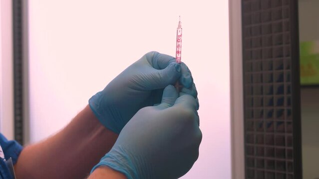 gloved doctor prepares a filled syringe for injection by tapping the syringe, ejecting a few drops from the hypodermic needle. Vaccination, immunization.