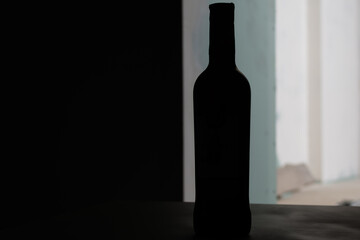 Dark silhouette of glass bottle in backdrop light on blurred background