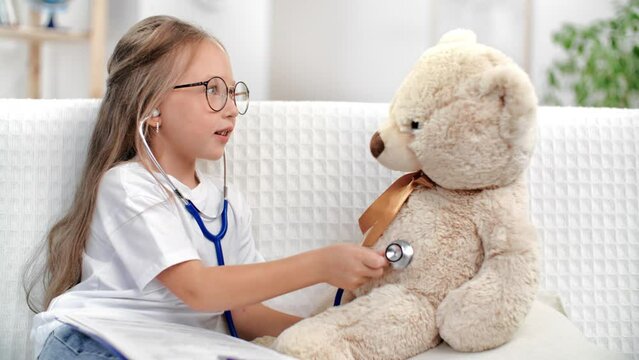 Adorable baby kid girl playing hospital medical doctor listening bear toy stethoscope at white room