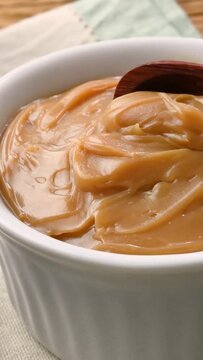 Vertical video. Hand getting doce de leite, traditional brazilian creamy milk sweet with bread and coffee over wooden table