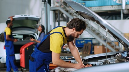 Mechanic in car service uses torque wrench to tighten bolts inside vehicle after fixing components inside. Repair shop employee utilizing professional tools to make sure automobile is properly working