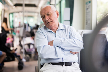 Senior European man sitting on seat inside tram and having a nap.