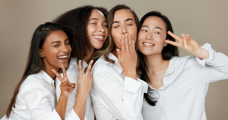 Diversity, peace sign and group of women in studio for empowerment, wellness and community. Emoji, friends and people hug, blow kiss and smile for beauty, inclusion and support on brown background