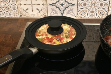 stewed vegetables with eggs in a frying pan with a silicone lid on an electric stove