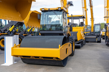New road roller for road construction and soil compaction and other construction equipment. Sale of new construction and municipal equipment at a dealership or fair. Heavy machinery