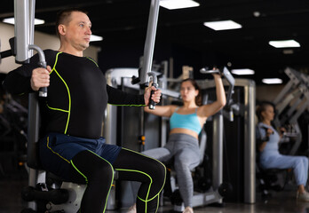 Portrait of concentrated adult man doing strength training in gym, performing chest muscles...