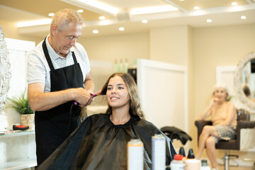 Fototapeta premium Professional male stylist cutting hair of happy girl in salon