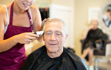 Young female hairdresser working hair clipper with older man