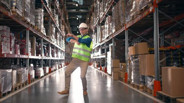 Industry man cheerfully dancing at storage building. Happy male worker having fun at warehouse. Industry employee celebrating professional success. Funny man waving hands at workplace.