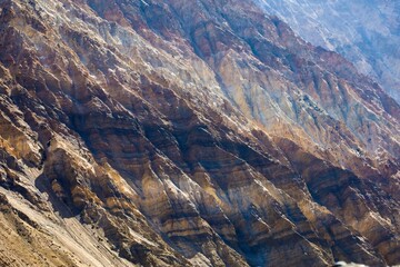 Close-up of Spiti Valley's rugged mountains in the Indian Himalayas, showcasing stratified layers, varied textures, and a vibrant color palette from browns to golds, highlighting geological wonders.