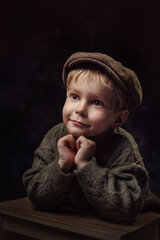 A little boy in a sweater and a retro-style cap on a dark background.