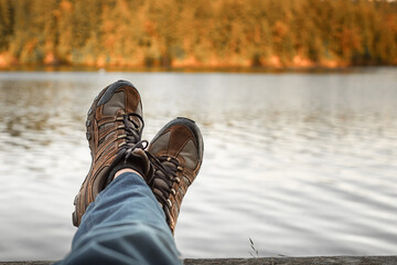 Man with hiking shoes relaxing by an autumn mountain lake. Adventure and people finding peace alone in nature  - obrazy, fototapety, plakaty