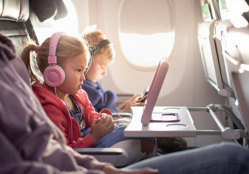Adorable little boy girl travel by plane. Cute Kids sit at the window of an airplane watching videos during the flight. Family Traveling abroad with children