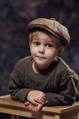 A little boy in a sweater and a retro-style cap on a dark background.