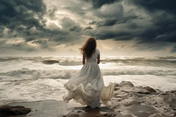 Foto op Plexiglas Back view of individual in white dress facing tumultuous sea waves under cloudy sky. Power of nature and tranquility. © Postproduction