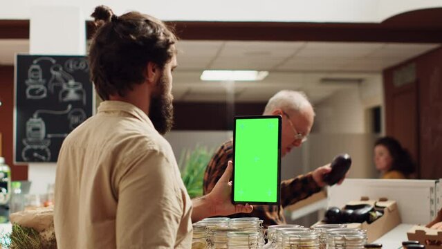 Man using isolated screen smartphone in zero waste supermarket to check ingredients for healthy recipe. Client in local grocery shop uses mockup mobile phone while shopping for organic veggies