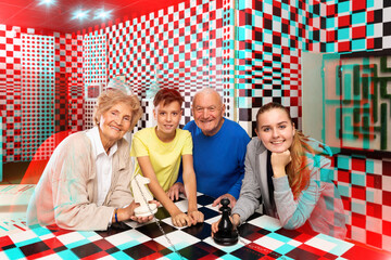 Group photo of positive grandparents and grandkids standing at big chess-board in escape room.