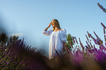Lavender fields near Lviv, Ukraine. Blooming lavender in summer. A girl in a white summer dress walks through lavender fields and touches lavender flowers with her hand. Selective focus