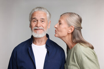 Senior woman kissing her beloved man on light grey background