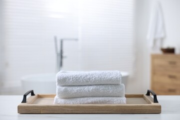 Wooden tray with stacked bath towels on white table in bathroom