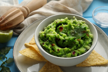 Delicious guacamole served with nachos chips on light blue table, closeup