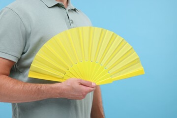 Man holding hand fan on light blue background, closeup