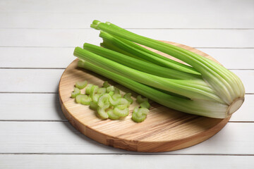 Board with fresh cut and whole celery on white wooden table, space for text