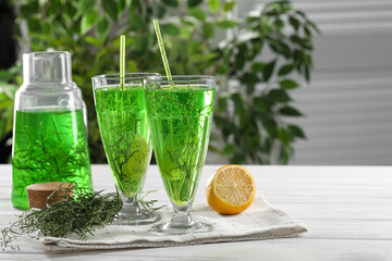 Glasses of homemade refreshing tarragon drink, sprigs and lemon on white wooden table, space for text