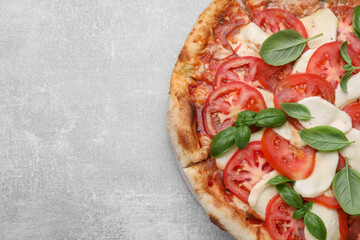 Delicious Caprese pizza with tomatoes, mozzarella and basil on light grey table, top view. Space...