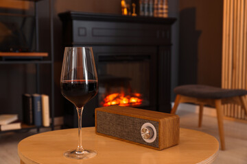 Glass of red wine and portable speaker on table in room. Relax at home