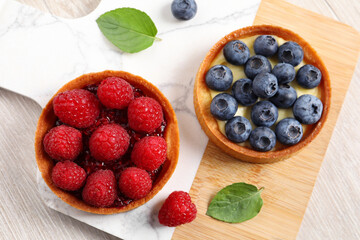 Tartlets with different fresh berries on light wooden table, top view. Delicious dessert