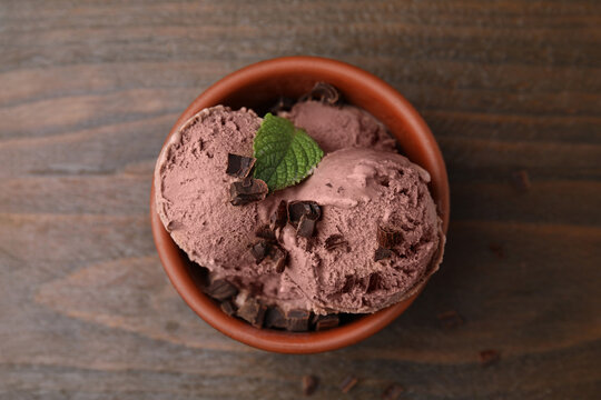 Bowl of tasty ice cream with chocolate chunks and mint on wooden table, top view