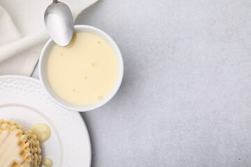 Tasty condensed milk, spoon and waffles on light grey table, flat lay. Space for text
