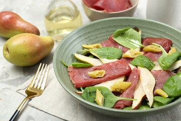 Delicious bresaola salad in bowl, fork and ingredients on light table, closeup