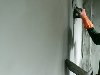 Hand wearing orange glove plastering the cement concrete on the wall. House construction building and renovation.